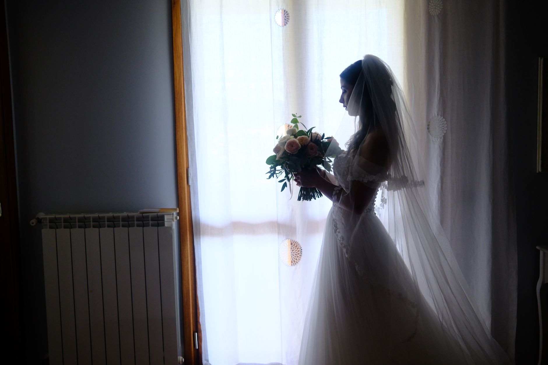 Silhouette einer Braut mit Blumenstrauß am Fenster